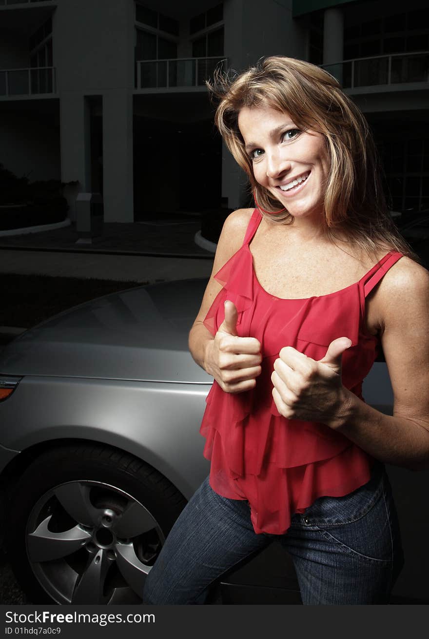 Woman posing by a luxury automobile and displaying a thumbs-up gesture. Woman posing by a luxury automobile and displaying a thumbs-up gesture