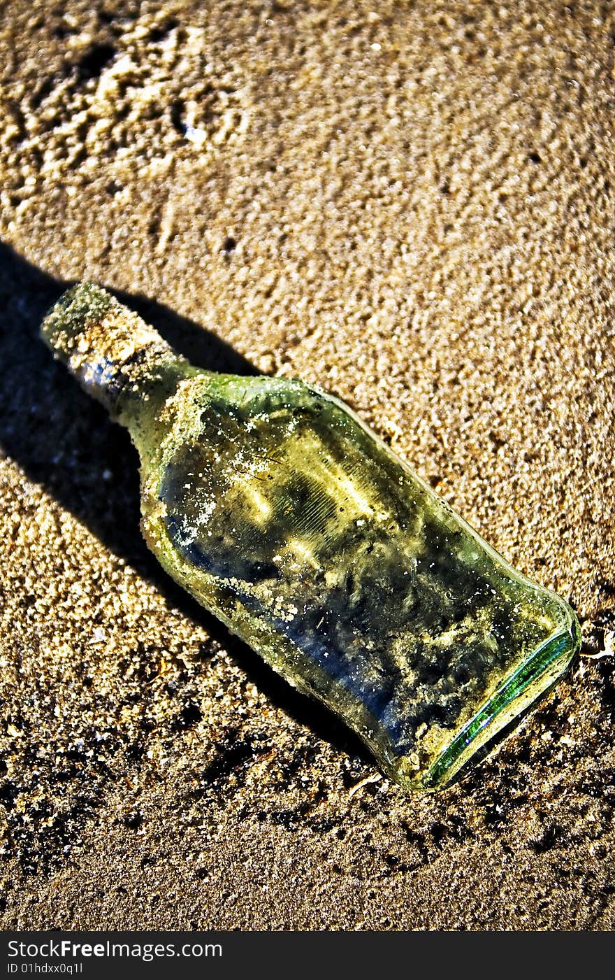 Green glass bottle in the sand. Green glass bottle in the sand.