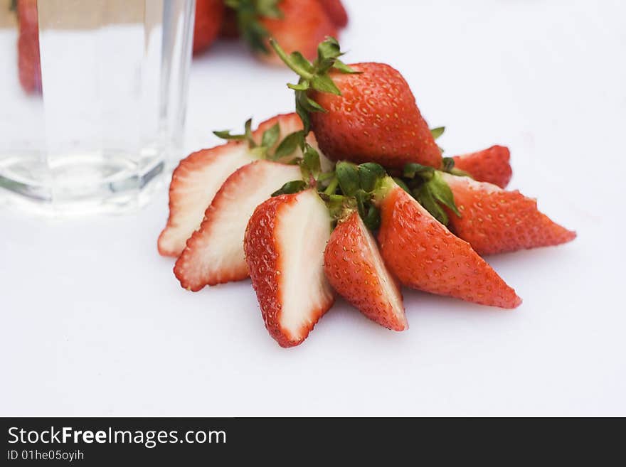 Some Strawberries have been cut in half and put into a circle. There are some whole strawberries in the background. There's also a glass of water. Some Strawberries have been cut in half and put into a circle. There are some whole strawberries in the background. There's also a glass of water