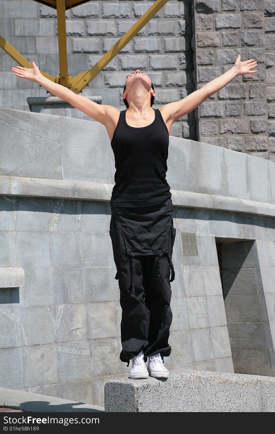 Beautiful brunette stands on stone block with raised hands