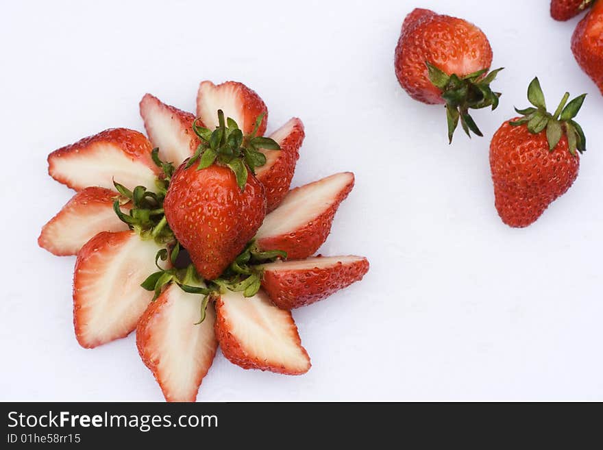 Some Strawberries have been cut in half and put into a circle. There are some whole strawberries in the background. Some Strawberries have been cut in half and put into a circle. There are some whole strawberries in the background.