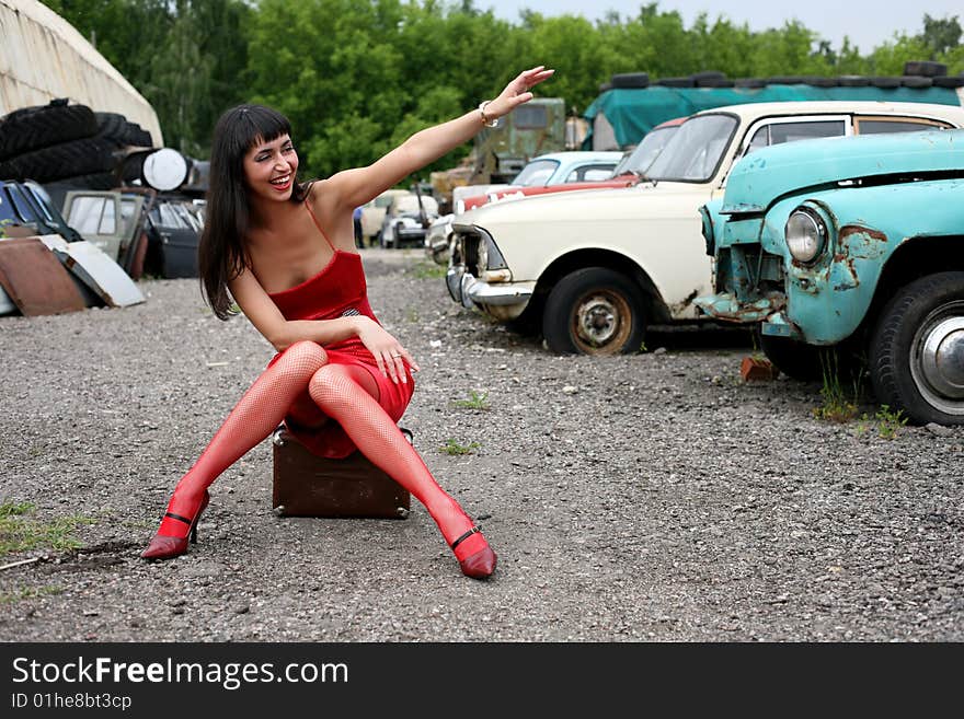 Girl sit atop vintage suitcase beside retro cars. Girl sit atop vintage suitcase beside retro cars