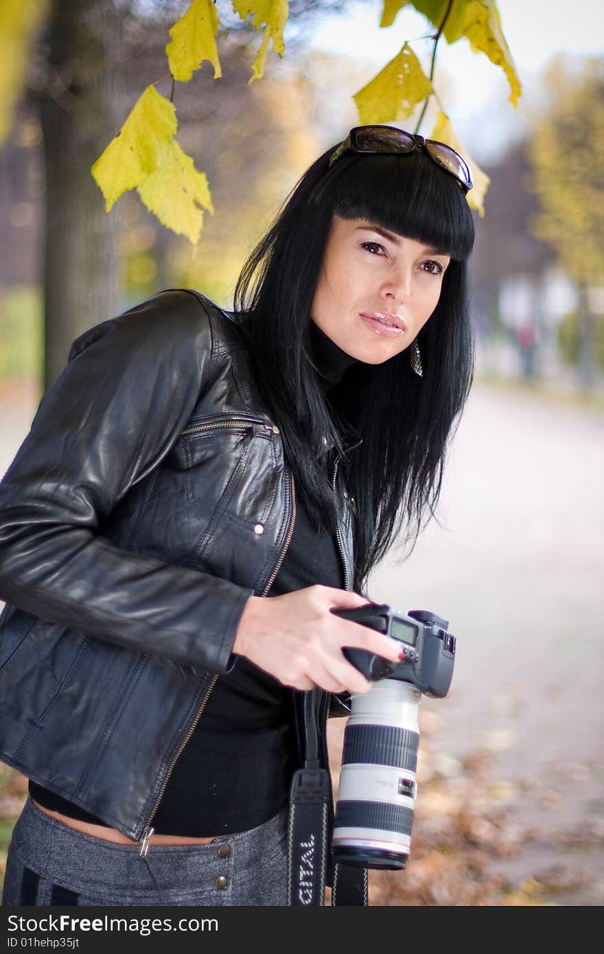 Portrait of beautiful fashion brunette girl in the park, holding photocamera