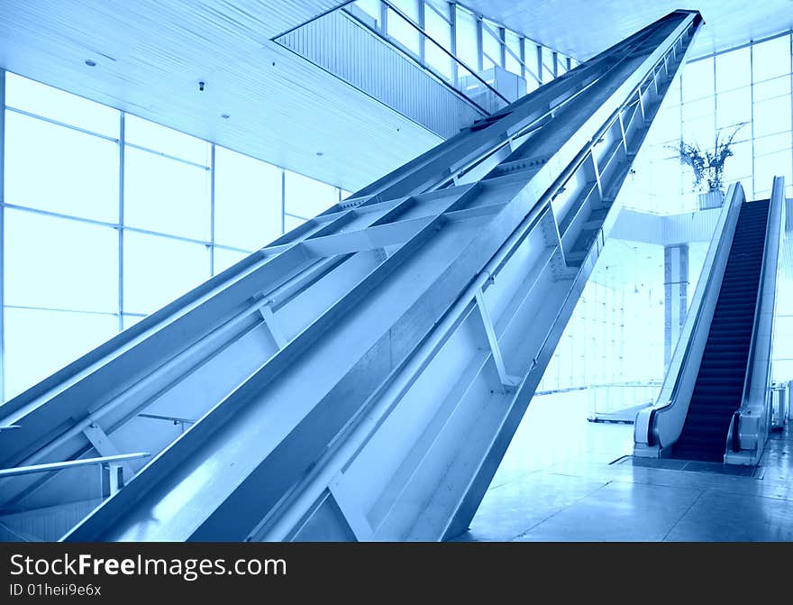 Glass hall with escalator on blue tones