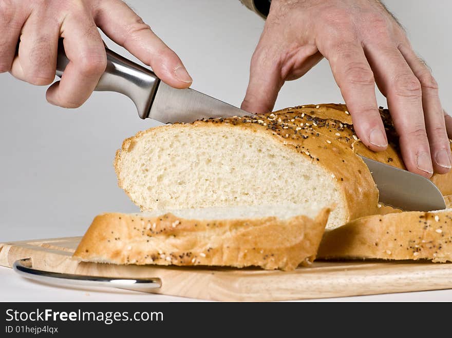 A man with long knife slicing through a large loaf of bread. A man with long knife slicing through a large loaf of bread.