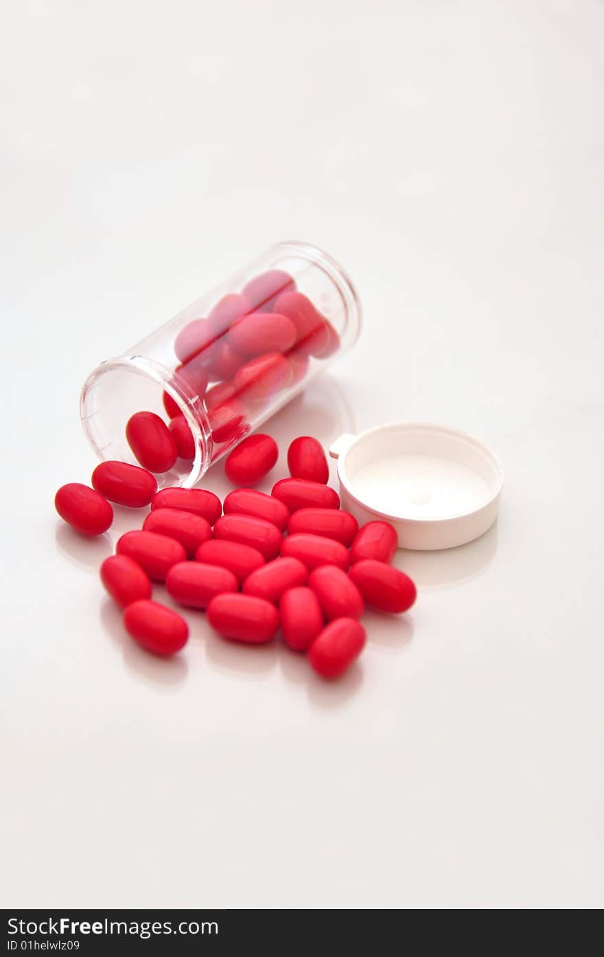 Small vile of pills spilled on top of a whit shiny table with red  pills. Small vile of pills spilled on top of a whit shiny table with red  pills.