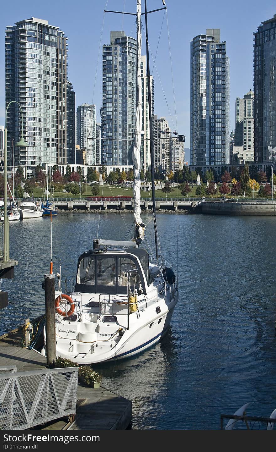 White sailboat docked in the harbor with the city skyline in the background.