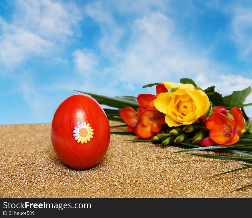 Easter spring celebration with red decorated egg, yellow rose and freesia flowers over golden sand and clear blue sky. Room for your text. Easter spring celebration with red decorated egg, yellow rose and freesia flowers over golden sand and clear blue sky. Room for your text.