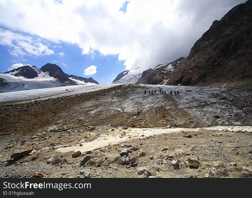 Trekkers and high mountains landscape in the alps during summer. The remains of a big glacier illustrating the global warming.