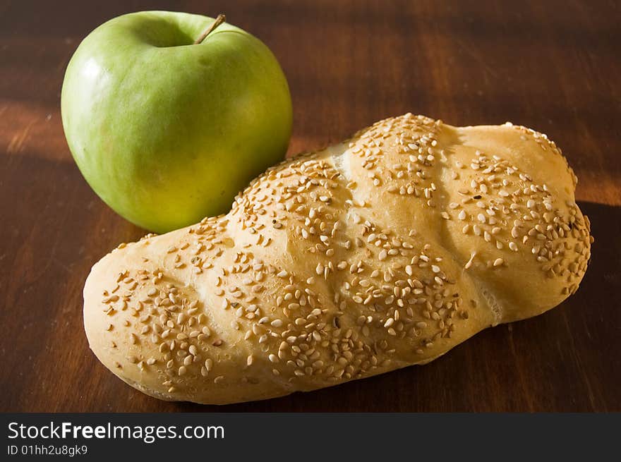 A bread loaf on a wooden table, with a green apple. A bread loaf on a wooden table, with a green apple