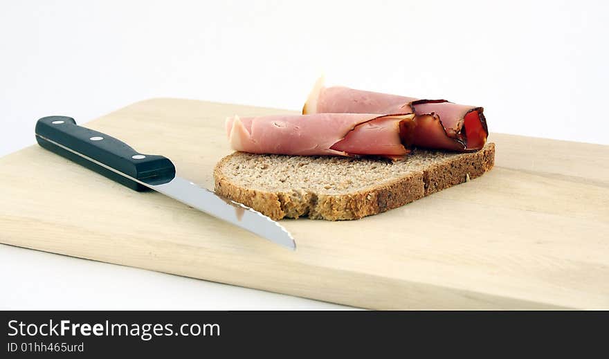 A slice of bread with ham presented on a wooden plate. A slice of bread with ham presented on a wooden plate