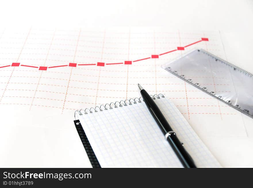 Empty page of a notepad with pen. A diagram and a ruler on the background. Empty page of a notepad with pen. A diagram and a ruler on the background.