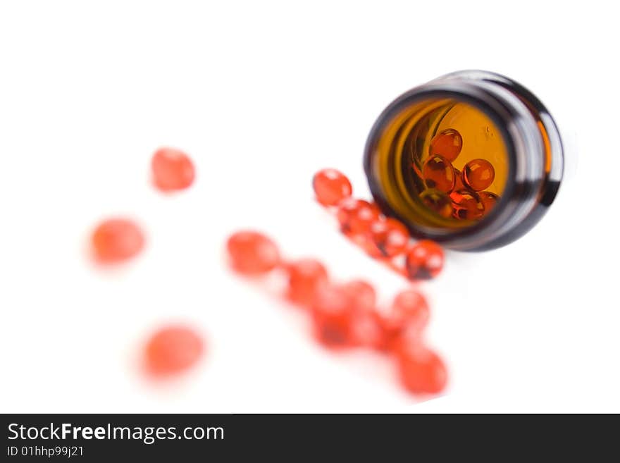 Glass bottle with red pills on white background