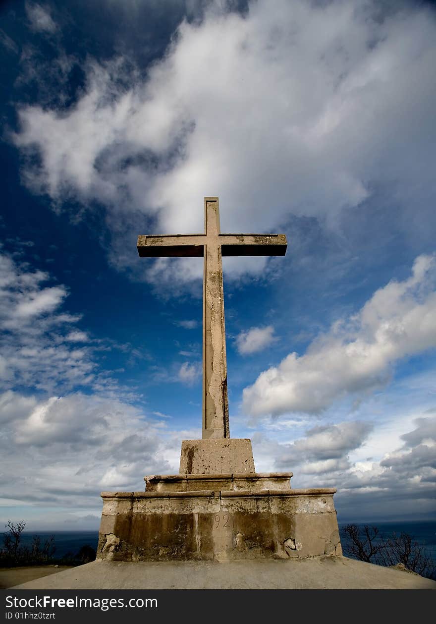 Cross made of stone on the top of the hill near the clouds pointing to the heaven above. Cross made of stone on the top of the hill near the clouds pointing to the heaven above