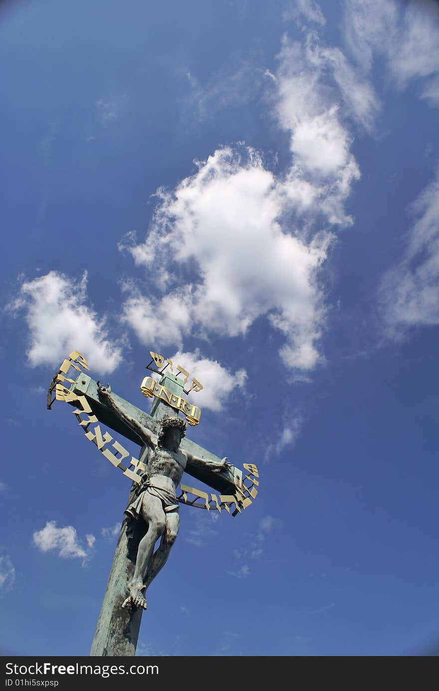 A large sculpted Jesus crucifix with gilded lettering and the blue cloudy sky in the background. On the Charles Bridge (Karlov Most) in Prague, Czech Republic. A large sculpted Jesus crucifix with gilded lettering and the blue cloudy sky in the background. On the Charles Bridge (Karlov Most) in Prague, Czech Republic.