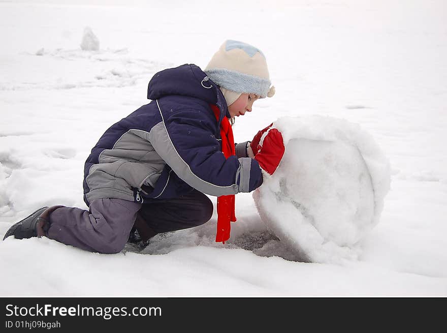 Little girl rolling snow ball for snowman