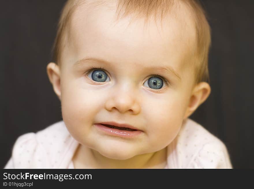 Portrait of a beautiful baby girl smiling and looking into the camera on a black background. Portrait of a beautiful baby girl smiling and looking into the camera on a black background