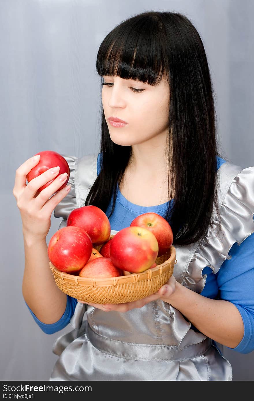 Beautiful girl holds in hands red apples on grey background