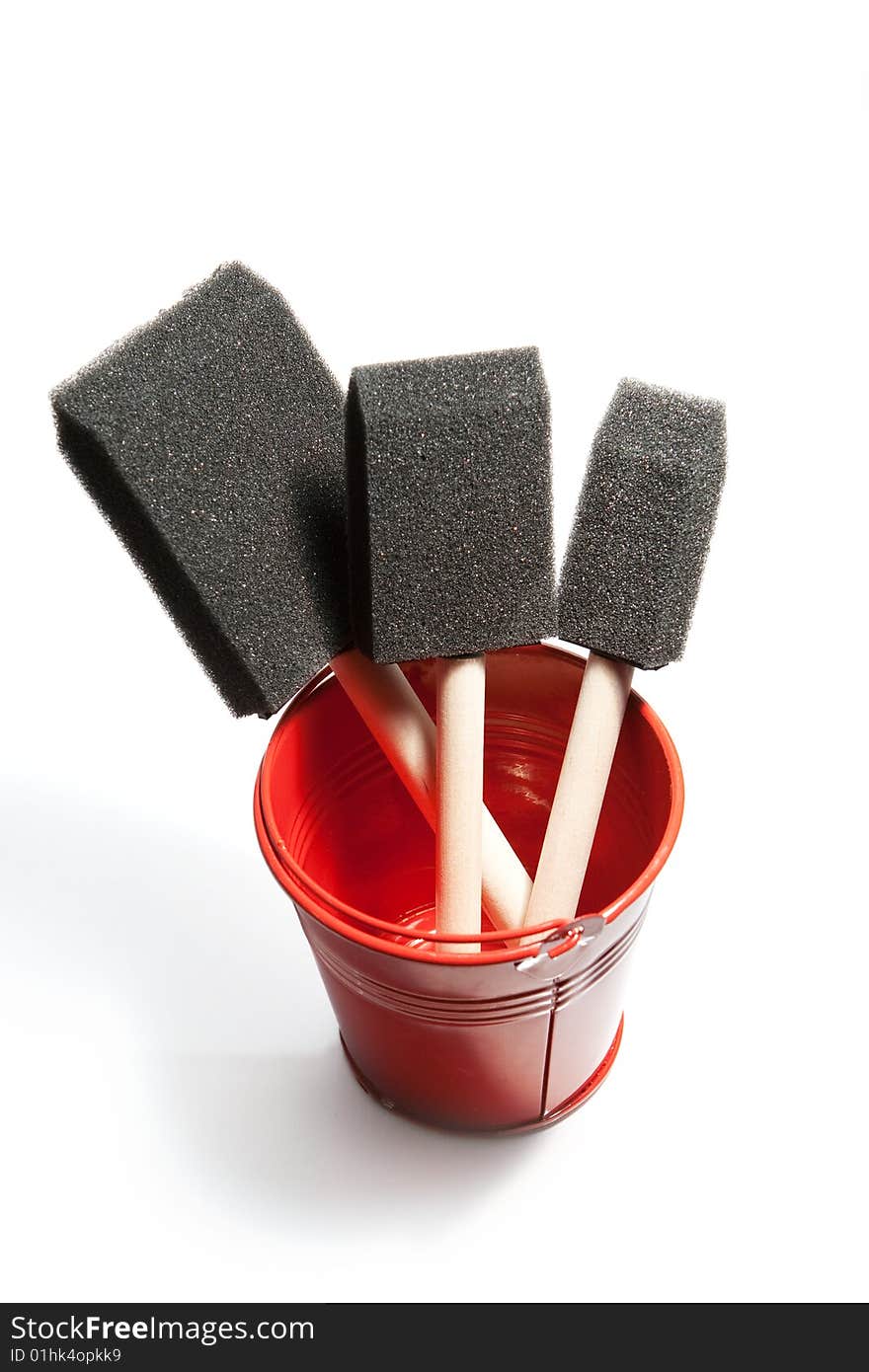 Shiny red bucket contains paint brushes.