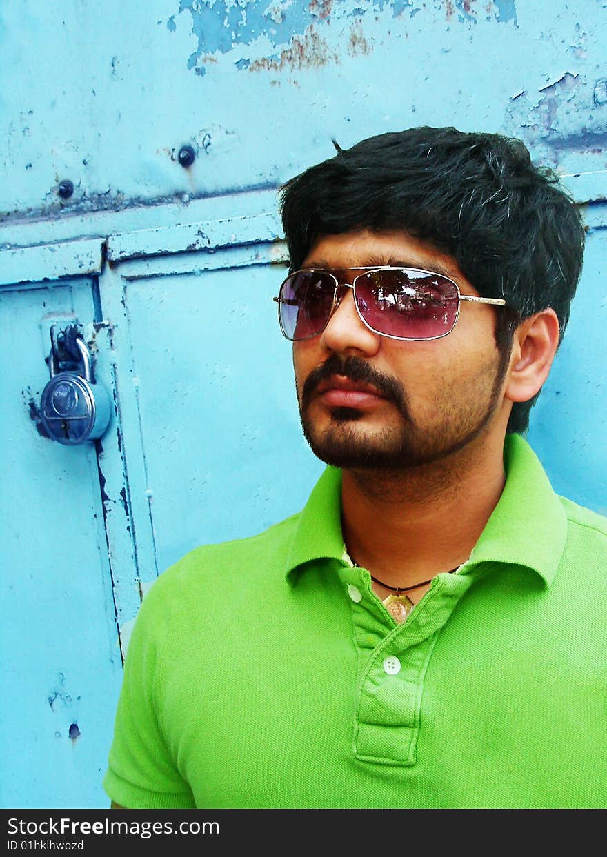 A stylish indian man with bright green t-shirt standing in front of a contrasting turquoise blue background