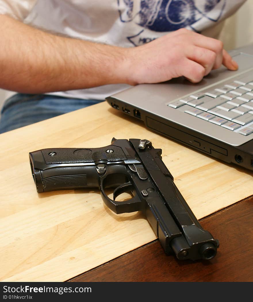 A man surfing the net with a hand gun by his side. A man surfing the net with a hand gun by his side