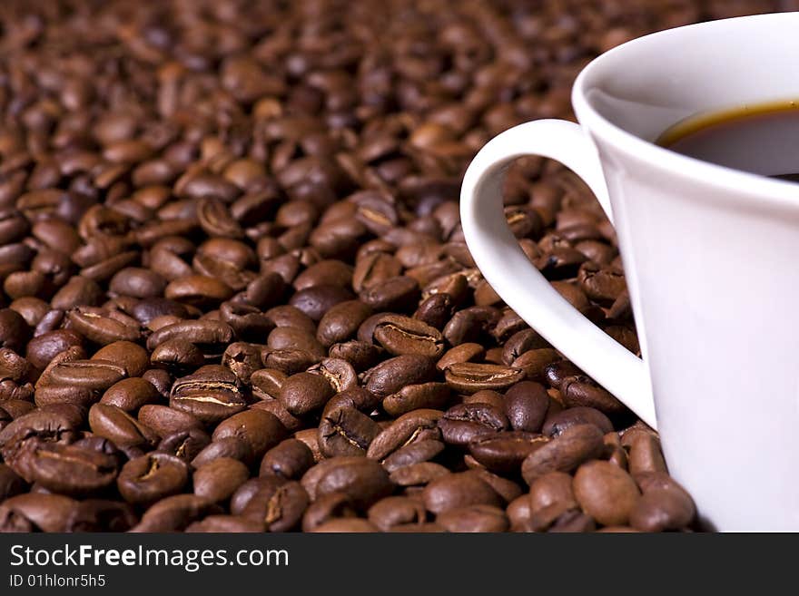 Shallow depth of field close-up of a freshly brewed cup of coffee on a bed of coffee beans. Shallow depth of field close-up of a freshly brewed cup of coffee on a bed of coffee beans