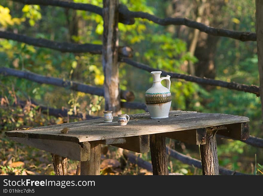 Rustic table wit water pot and two noggins in morning sunlight