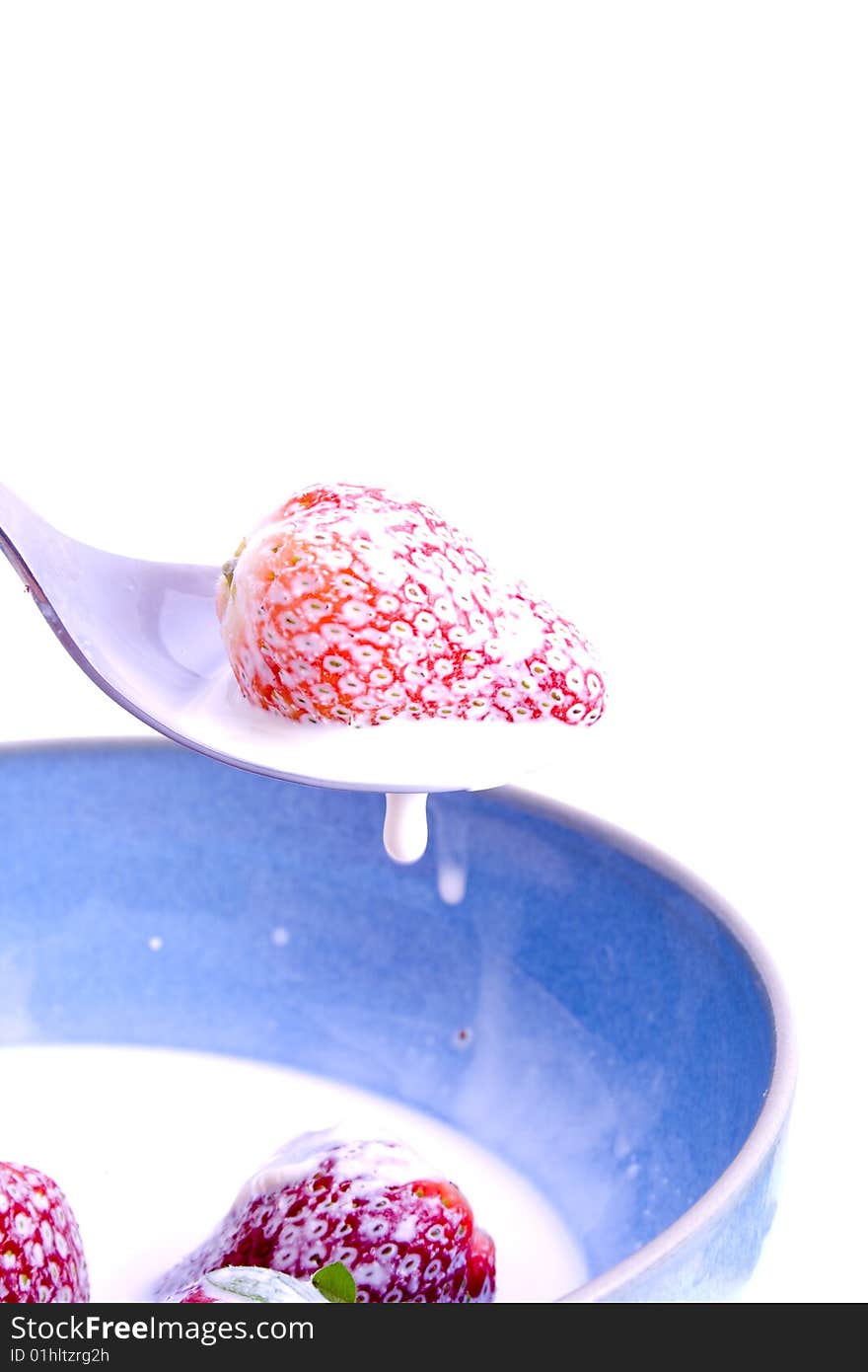 A spoon over a bowl of strawberries and cream. A spoon over a bowl of strawberries and cream