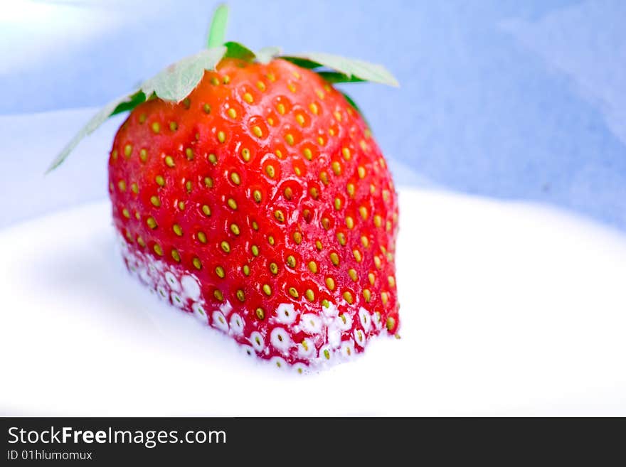 A fresh strawberry resting in a bowl of cream. A fresh strawberry resting in a bowl of cream