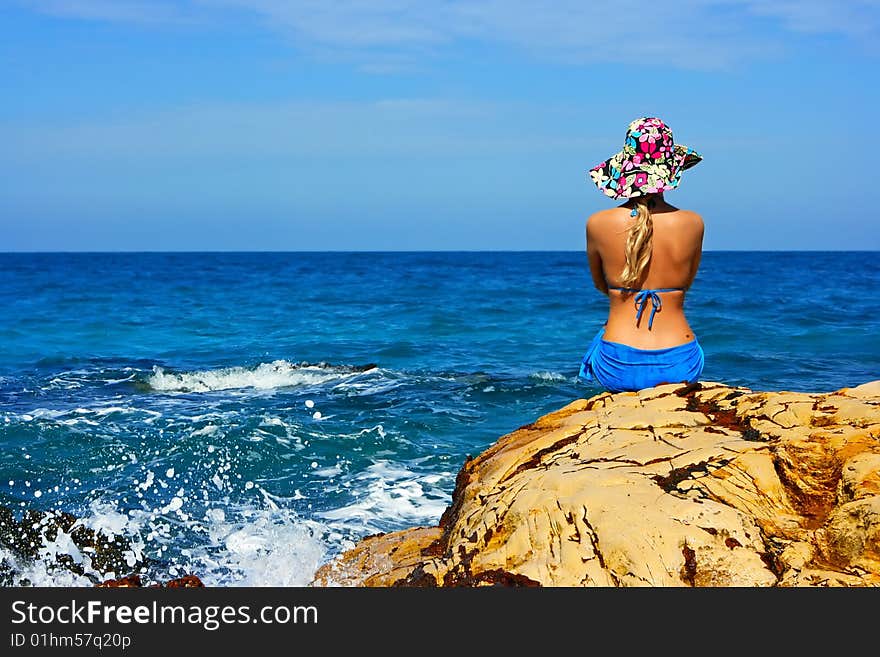 Girl in hat sitting on the rocks at the sea. Girl in hat sitting on the rocks at the sea