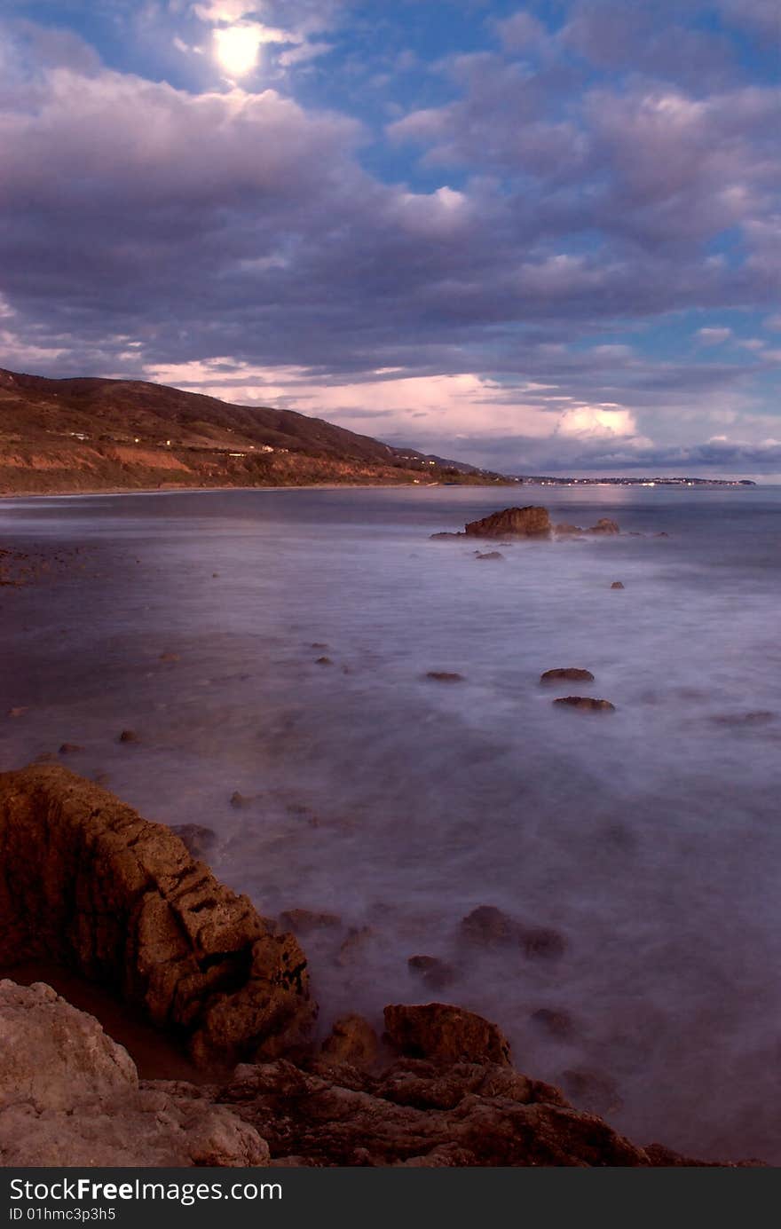 Leo Carillo Beach, in Southern California, at dusk with a full moon, cloudy sky and sharp rocks in the low tide. Leo Carillo Beach, in Southern California, at dusk with a full moon, cloudy sky and sharp rocks in the low tide