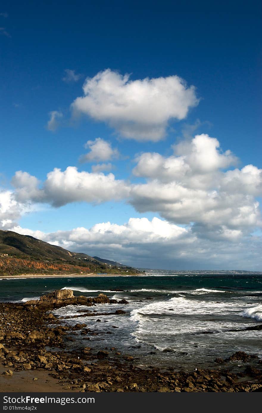 The rocky shore of Leo Carillo Beach in Southern California, with mountains in the background and white clouds in the sky. The rocky shore of Leo Carillo Beach in Southern California, with mountains in the background and white clouds in the sky