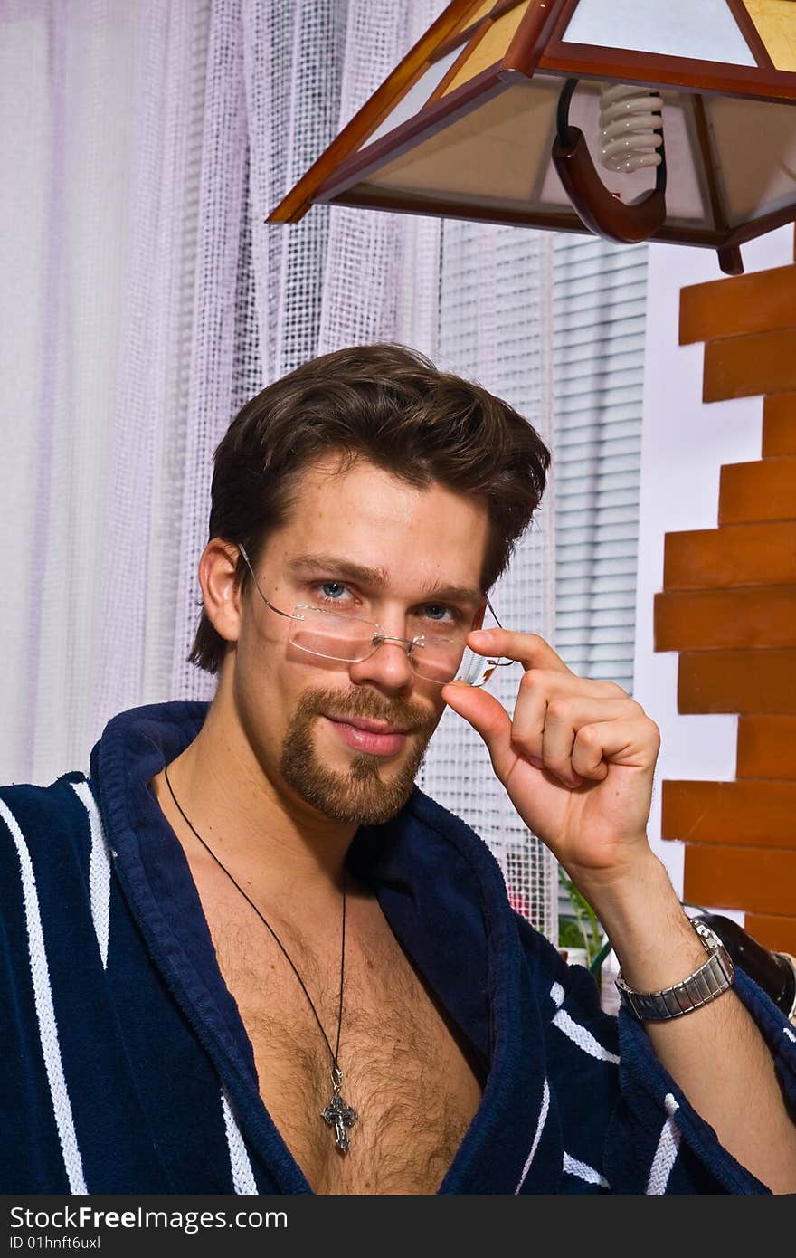 Young man wearing blue striped bathrobe puts on his glasses. Young man wearing blue striped bathrobe puts on his glasses