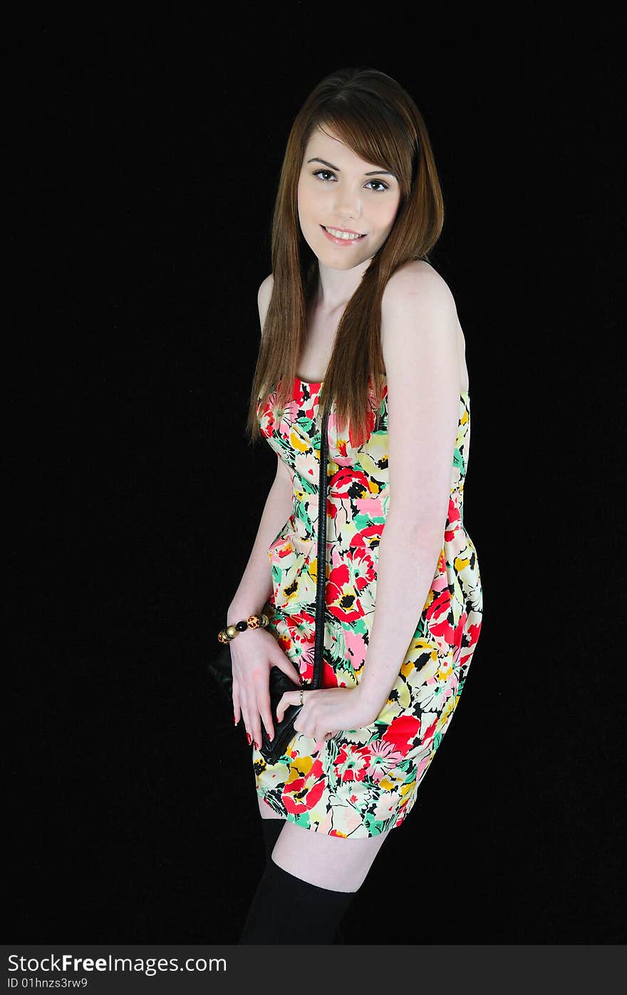 Female model standing against a black back drop smiling at the camera wearing a flower pattern dress. Female model standing against a black back drop smiling at the camera wearing a flower pattern dress