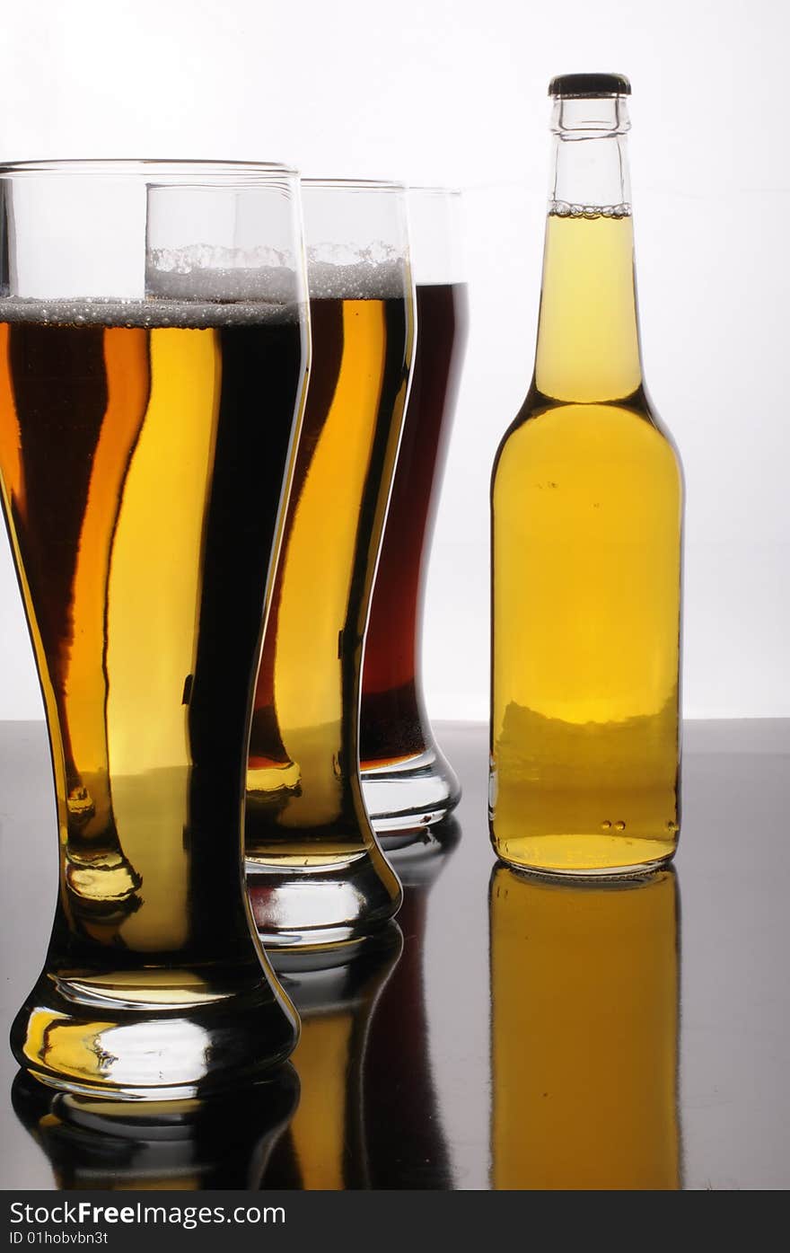 A bottle and three glasses of tasty light, gold, and dark beer. A bottle and three glasses of tasty light, gold, and dark beer