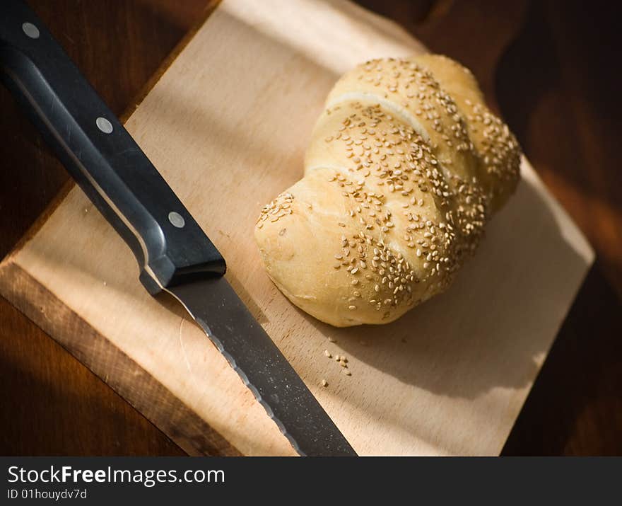 A bread loaf on a wooden table, with a knife ready. A bread loaf on a wooden table, with a knife ready