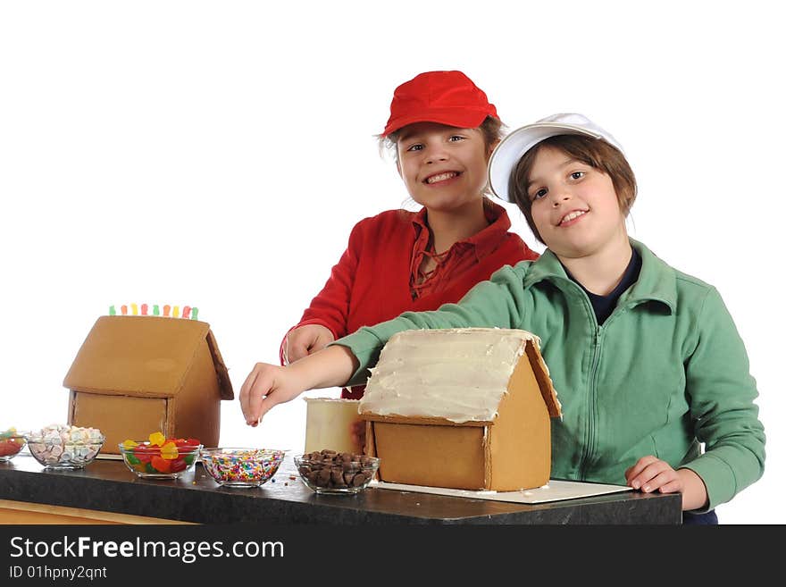 Two girls delighted to be making gingerbread houses for the holidays.  Isolated on white.