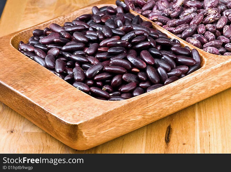 A couple of dark red and spotted kidney beans in wooden dish