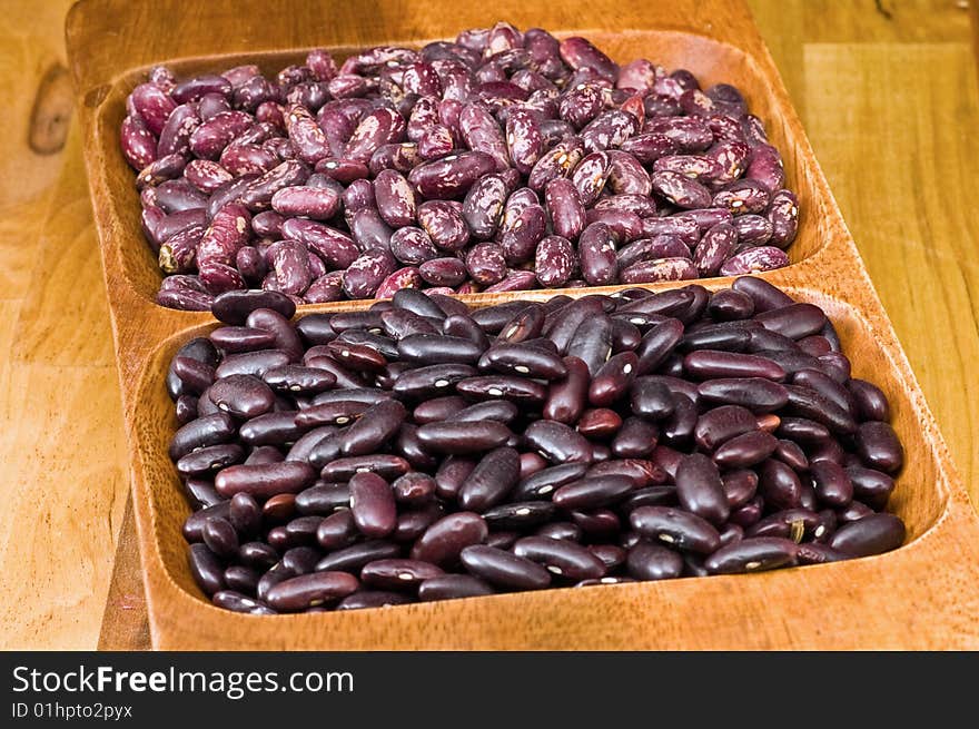 A couple of dark red and spotted kidney beans in wooden dish