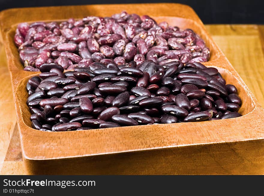 A couple of dark red and spotted kidney beans in wooden dish