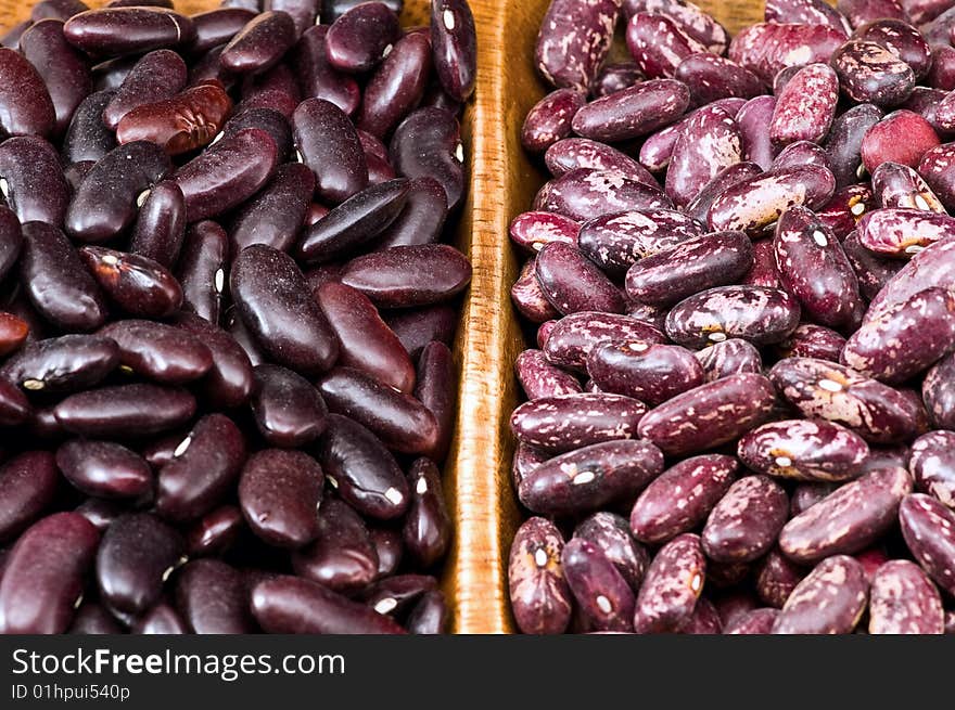 A couple of dark red and spotted kidney beans in wooden dish