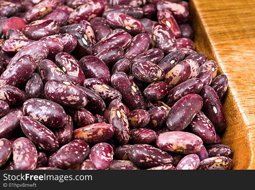 A couple of dark red and spotted kidney beans in wooden dish