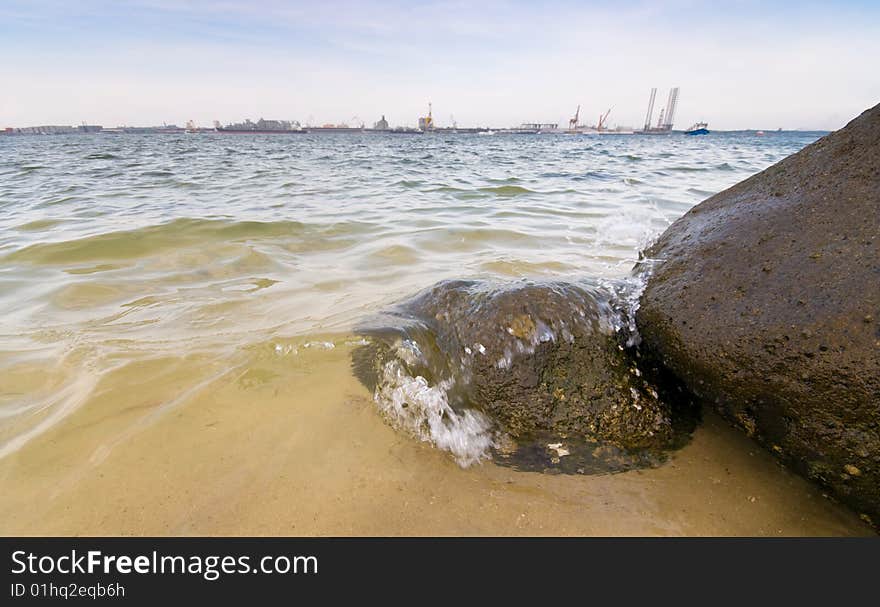 View across a straits of an industrial and port complex from a rocky beach