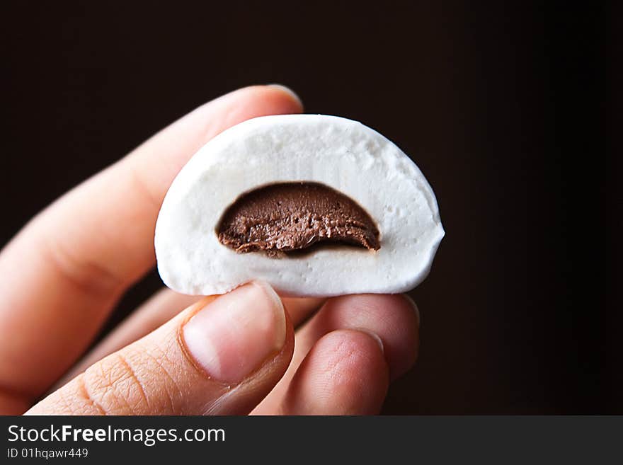 Marshmallow with chocolate inside in a hand. Isolated on black background. Marshmallow with chocolate inside in a hand. Isolated on black background