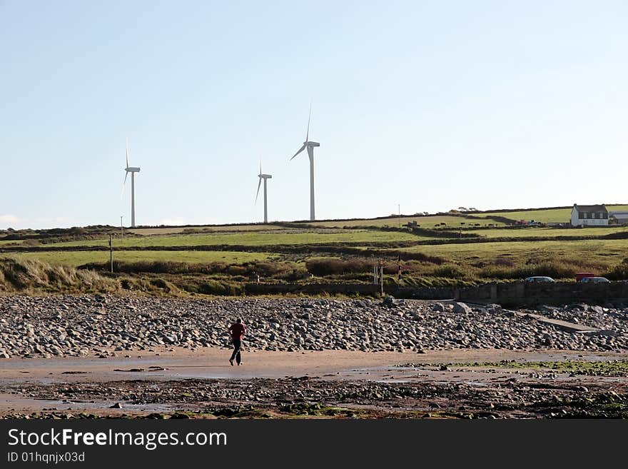 Man running on beale beach co kerry ireland on a cold winters morning with turbines in the background. Man running on beale beach co kerry ireland on a cold winters morning with turbines in the background