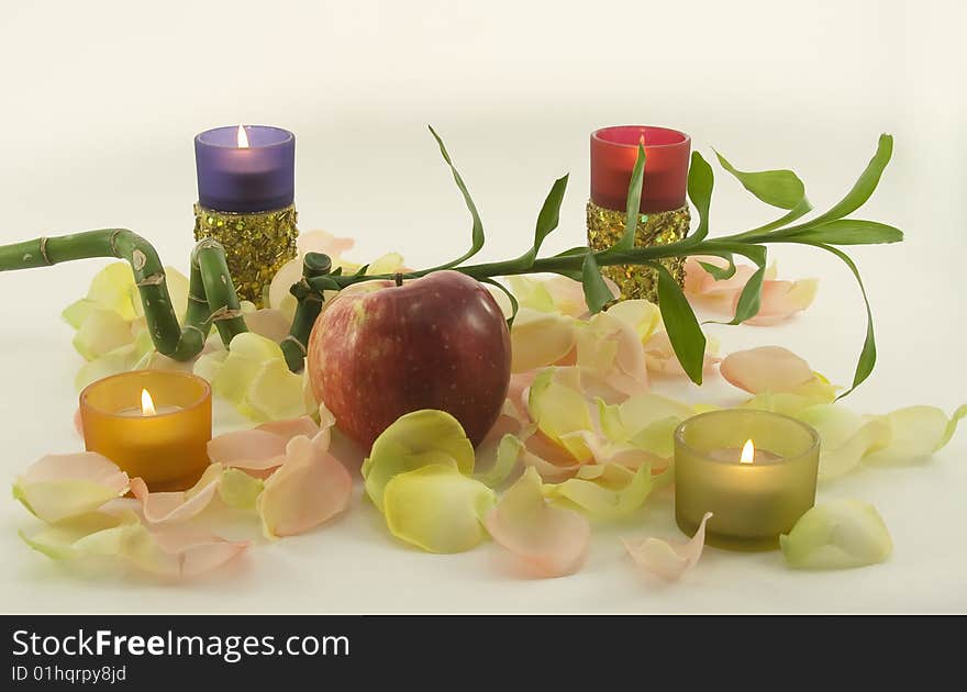 Bamboo and big red fresh apple with aromatic rose leave in rays of color candles. Bamboo and big red fresh apple with aromatic rose leave in rays of color candles