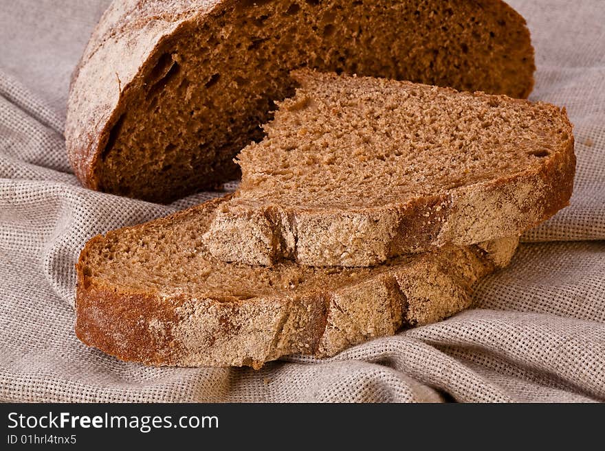 Sliced rustic brown bread loaf on the table covered with canvas tablecloth