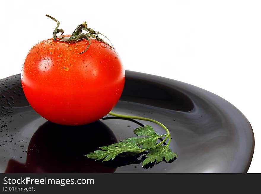 Wet red tomato with fresh parsley on the black plate. White background.