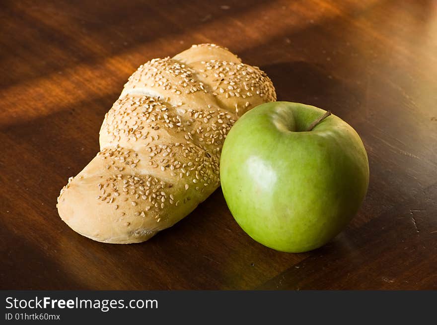 A bread loaf on a wooden table, with a green apple. A bread loaf on a wooden table, with a green apple