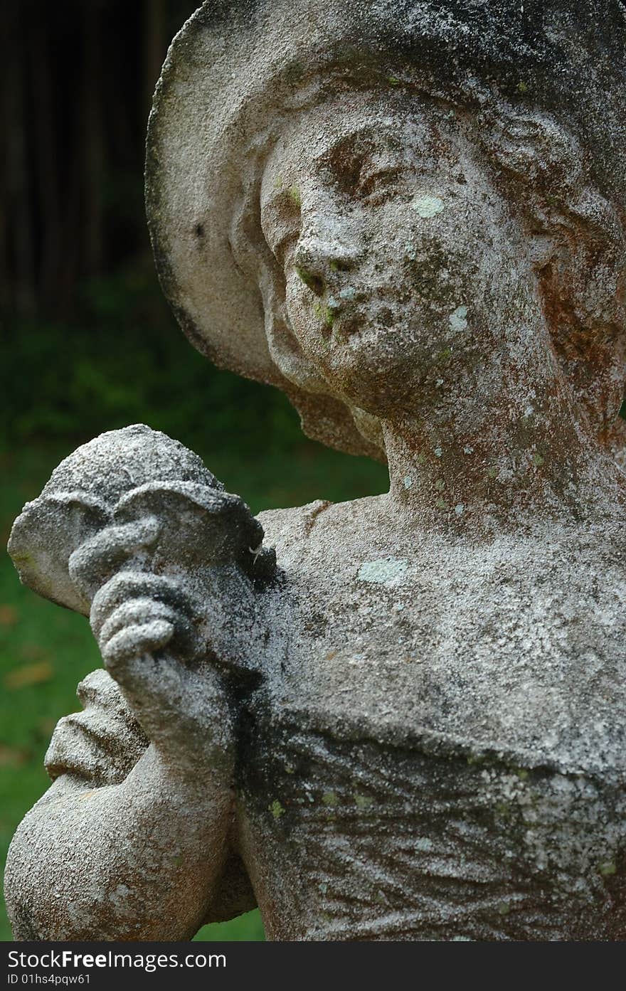 An old weathered statue of a lady holding a flower